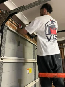Technician repairing a garage door spring, wearing a branded Vibe Garage Door Repair shirt.
