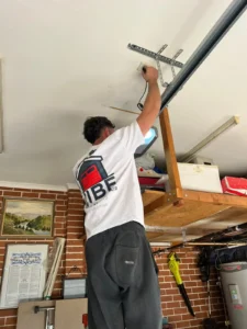Technician inspecting a garage door opener, wearing a Vibe Garage Door Repair company shirt.
