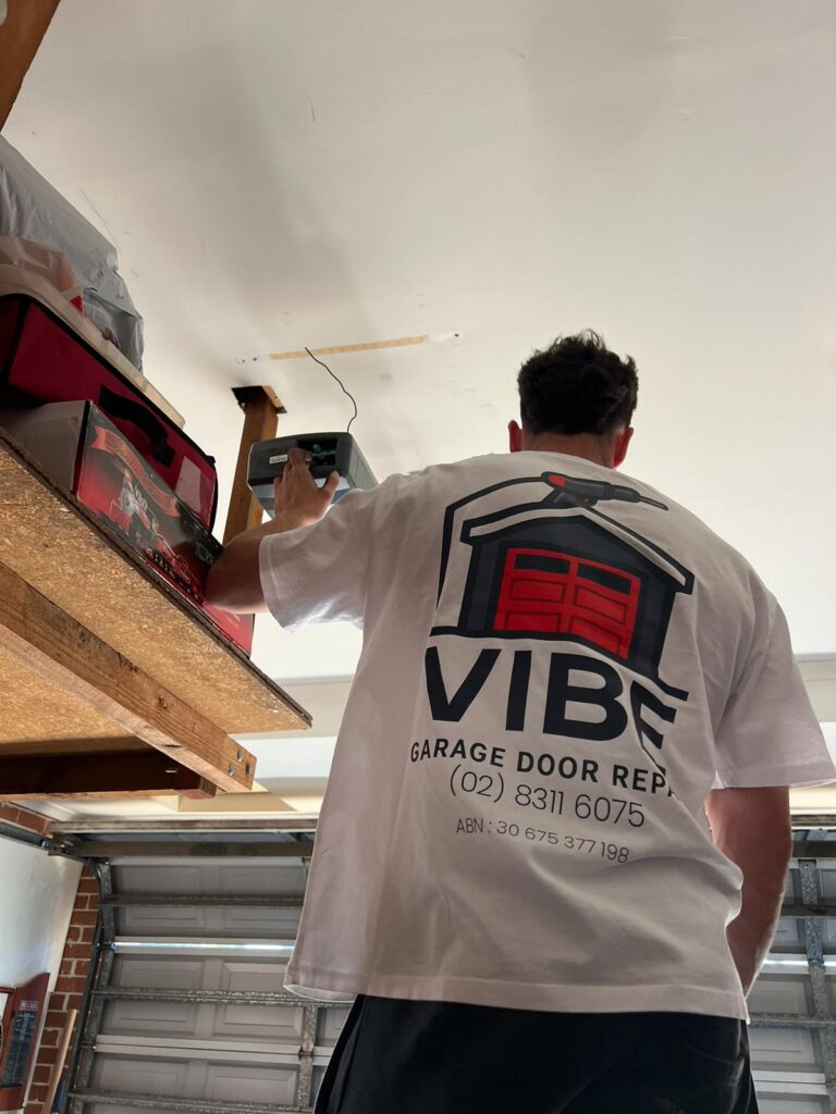 Technician repairing a garage door opener, wearing a branded Vibe Garage Door Repair shirt.