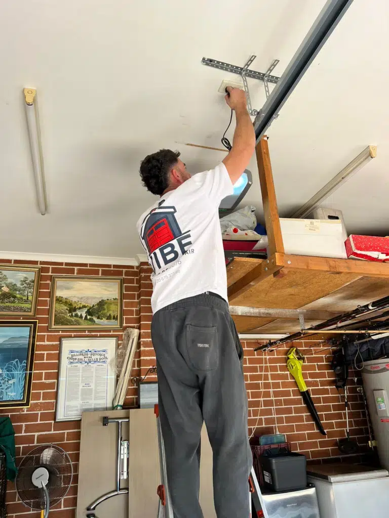 Vibe Garage Door Repair technician standing on a ladder performing garage door opener repair inside a residential garage in Sydney