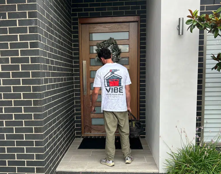 Vibe Garage Door Repair technician in branded uniform with tool bag at modern home front door for garage door service call.